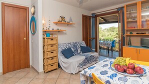 Un salon chaleureux avec un canapé, des meubles en osier, une table à manger ornée de fruits et un téléviseur placé dans un meuble en bois.