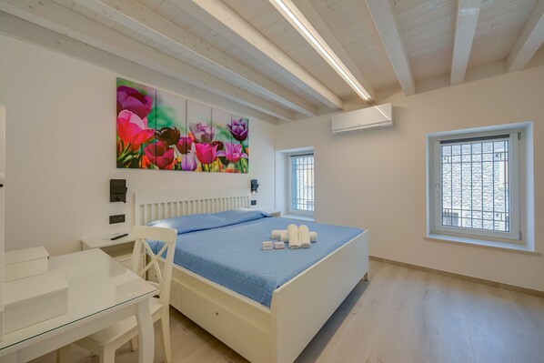 A bedroom with a bed, a desk, and a painting of flowers on the wall.