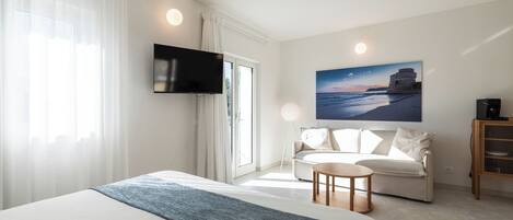 Habitación de hotel con cama, sofá, televisión montada en la pared y un cuadro de una escena costera.