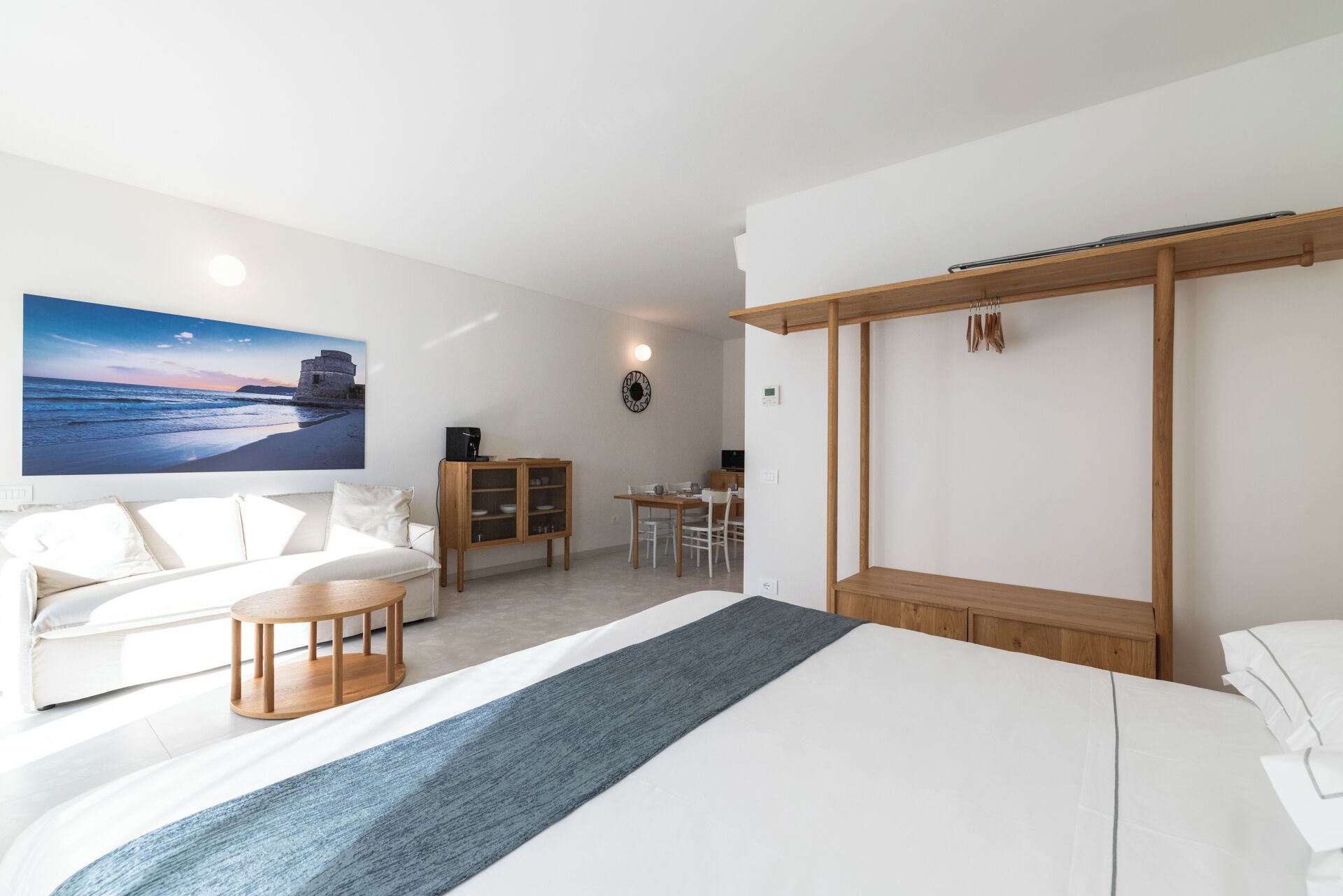 A modern hotel room with a large bed, a sofa, a dining table, and a TV displaying a scenic view.