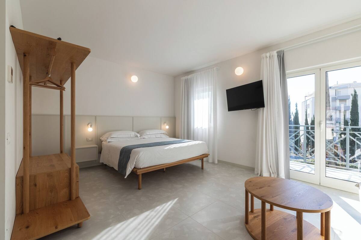 Una habitación de hotel moderna con una cama, un banco de madera, una mesita y un televisor montado en la pared.