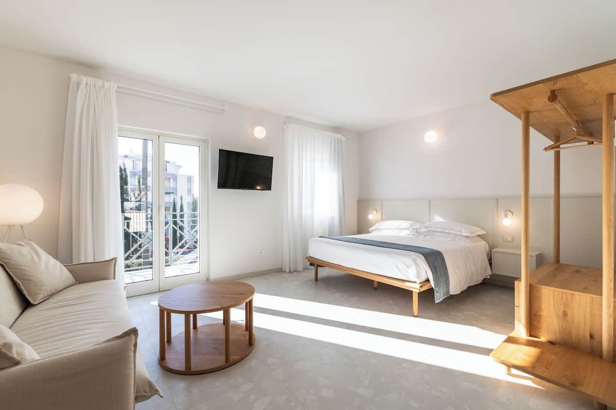 Una habitación de hotel moderna con una cama, una mesa redonda de madera, un sofá y un televisor fijado a la pared.
