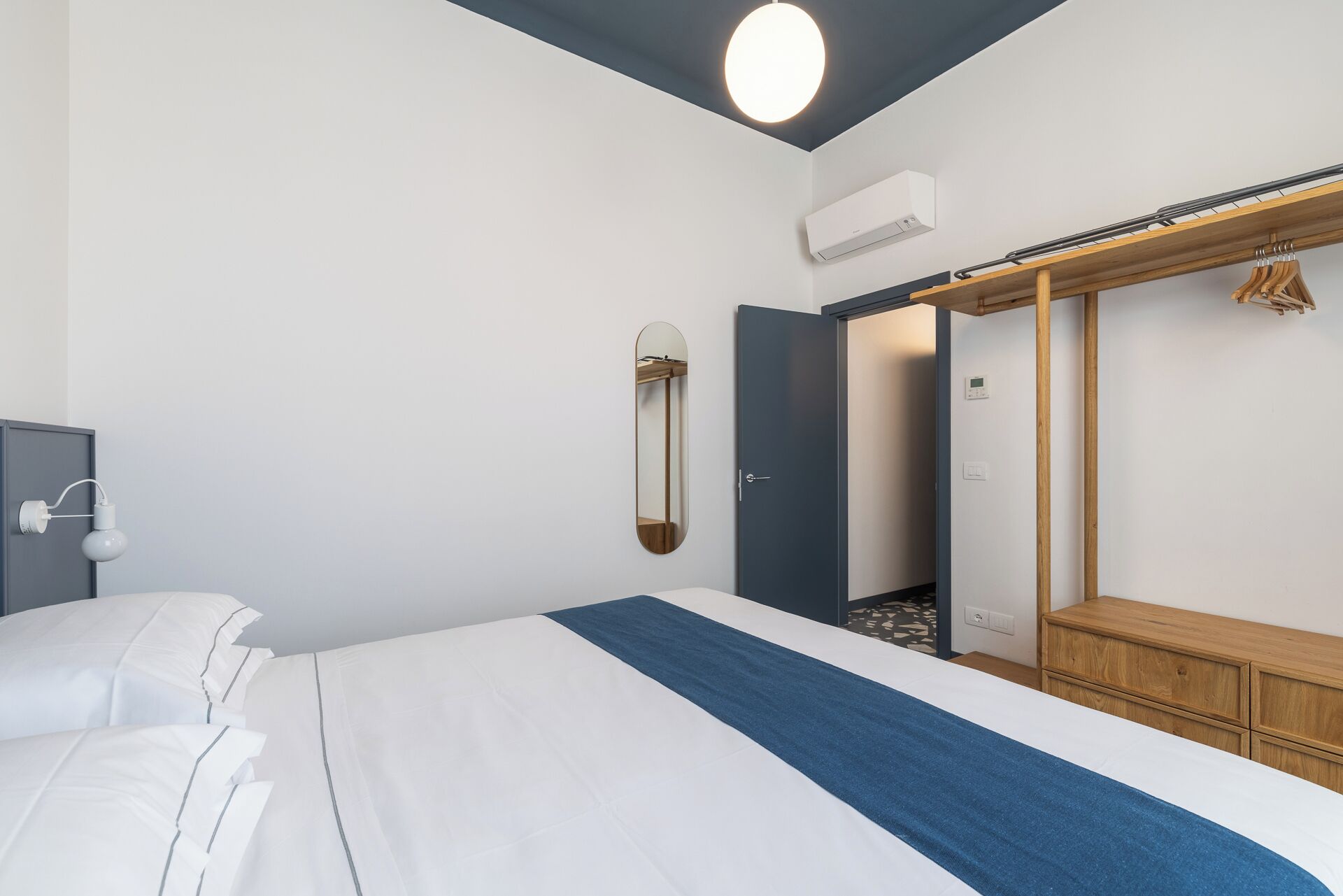 A modern hotel room with a bed, a wardrobe, a mirror, and an air conditioning unit.