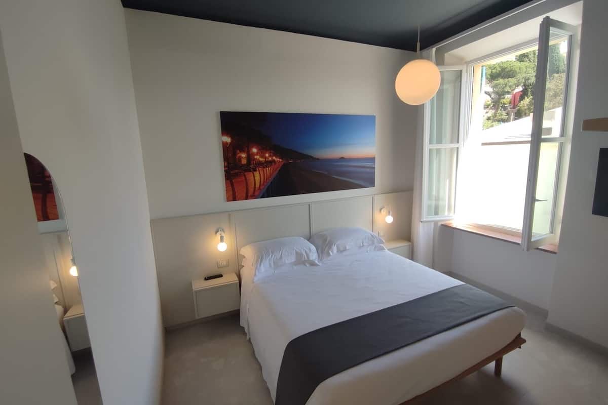 Un dormitorio con una cama grande, una mesita de noche, una lámpara de pared y una ventana con vistas al exterior.