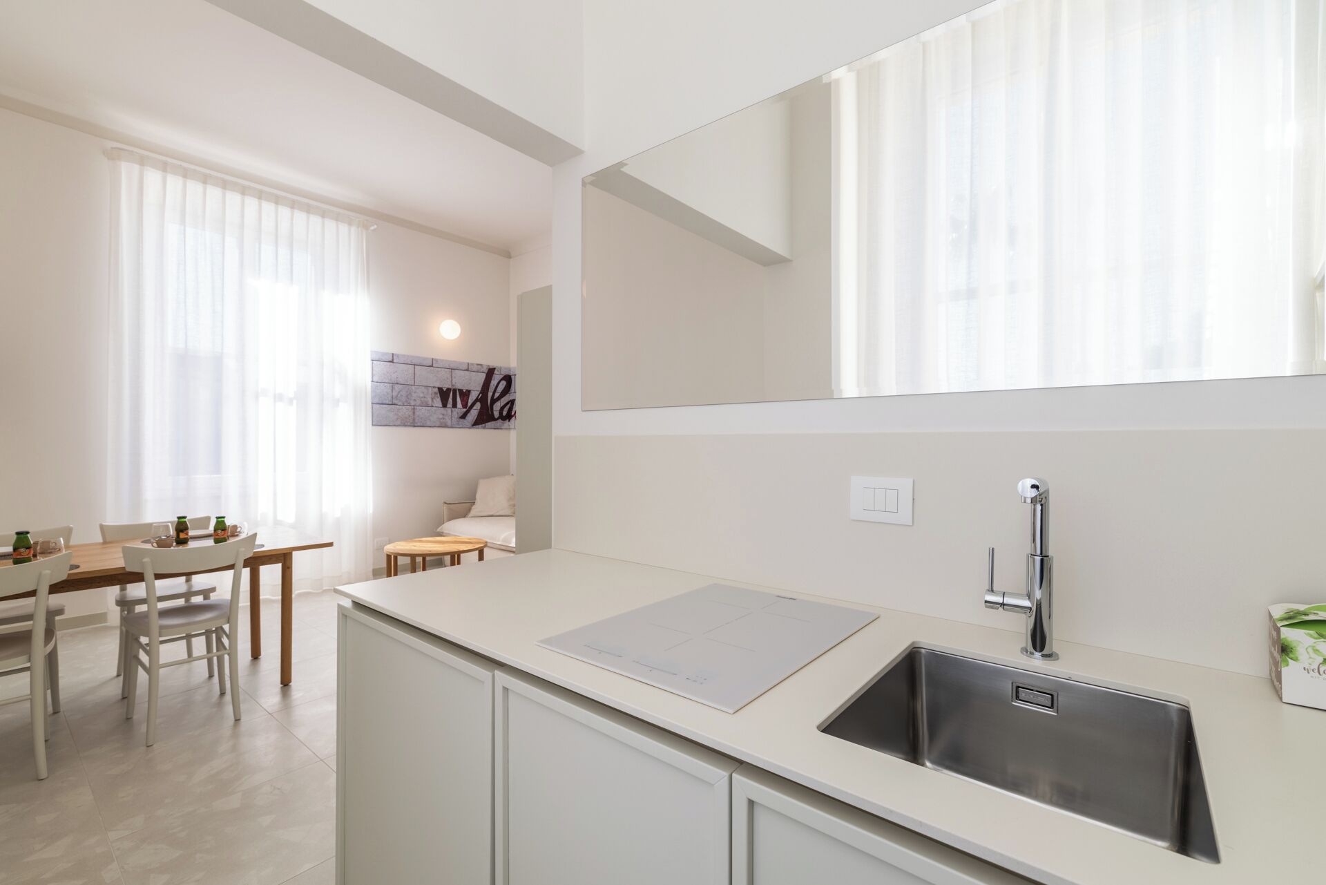 Uma cozinha moderna com pia embutida, área de jantar com mesa e cadeiras, e uma janela grande com cortinas leves.