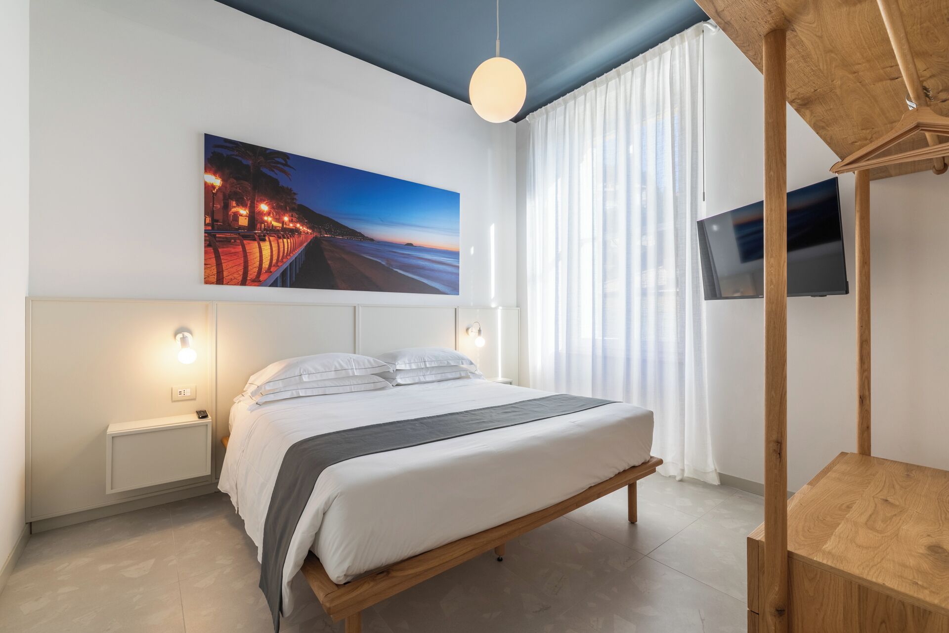 Ein modernes Schlafzimmer mit einem Bett, Nachttischen, einem Fernseher und einem großen Fenster mit Vorhängen.