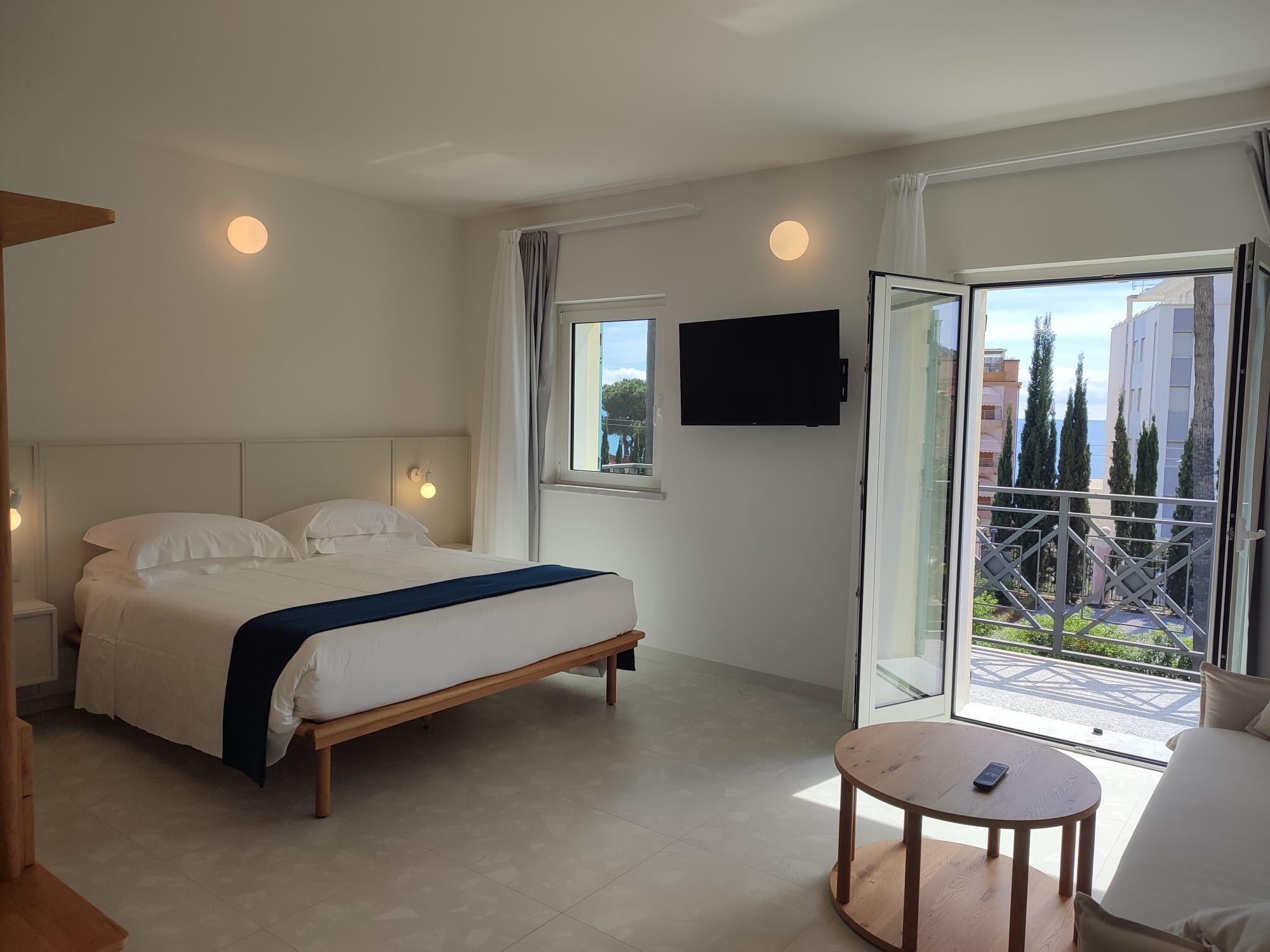 A hotel room with a bed, a TV, a balcony with a view, and a small table.