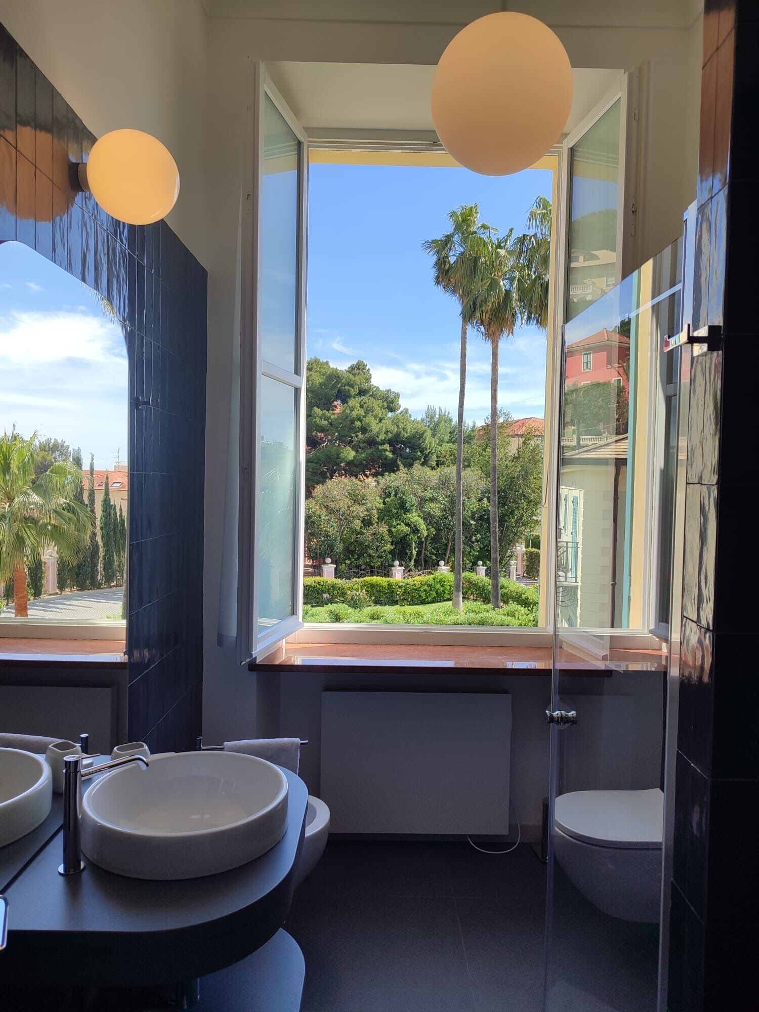 A modern bathroom with a large window, two sinks, and a toilet.