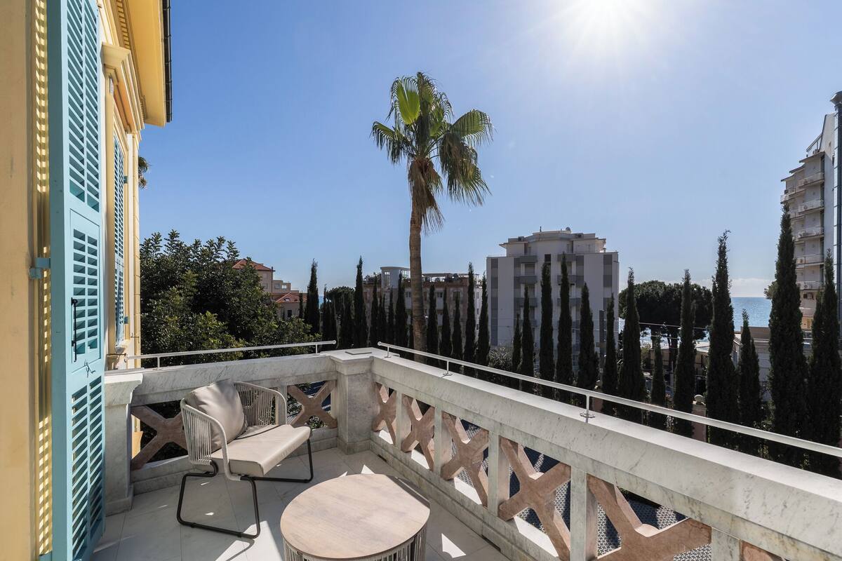 Un balcón con vista al mar, una palmera y edificios modernos.