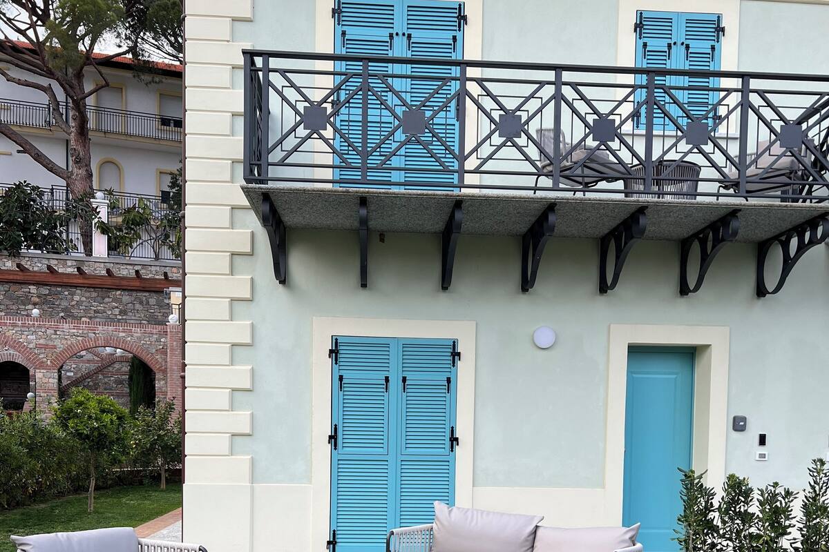 Un patio con mobiliario exterior, una puerta azul y un balcón con contraventanas azules.