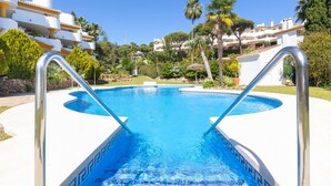 A swimming pool with clear blue water, surrounded by a white pool deck and metal pool ladders. - Calahonda Golf in Calahonda (Mijas)