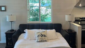 Une chambre dotée d’un grand lit, d’un lustre, d’une fenêtre donnant sur un paysage verdoyant, d’une table de chevet avec une lampe et d’un coin cuisine.