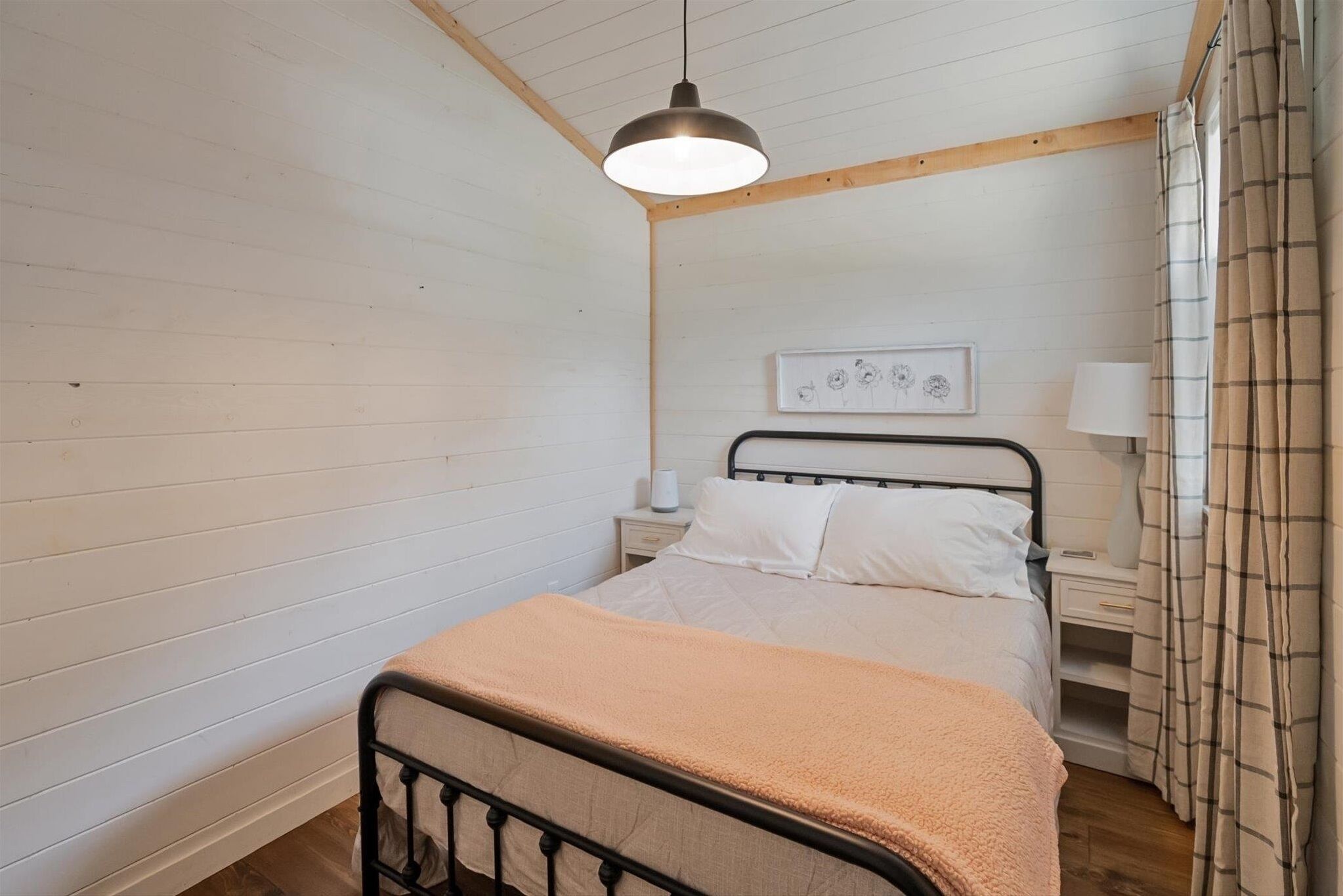 A bedroom with a bed, bedside table, lamp, and a hanging light fixture.