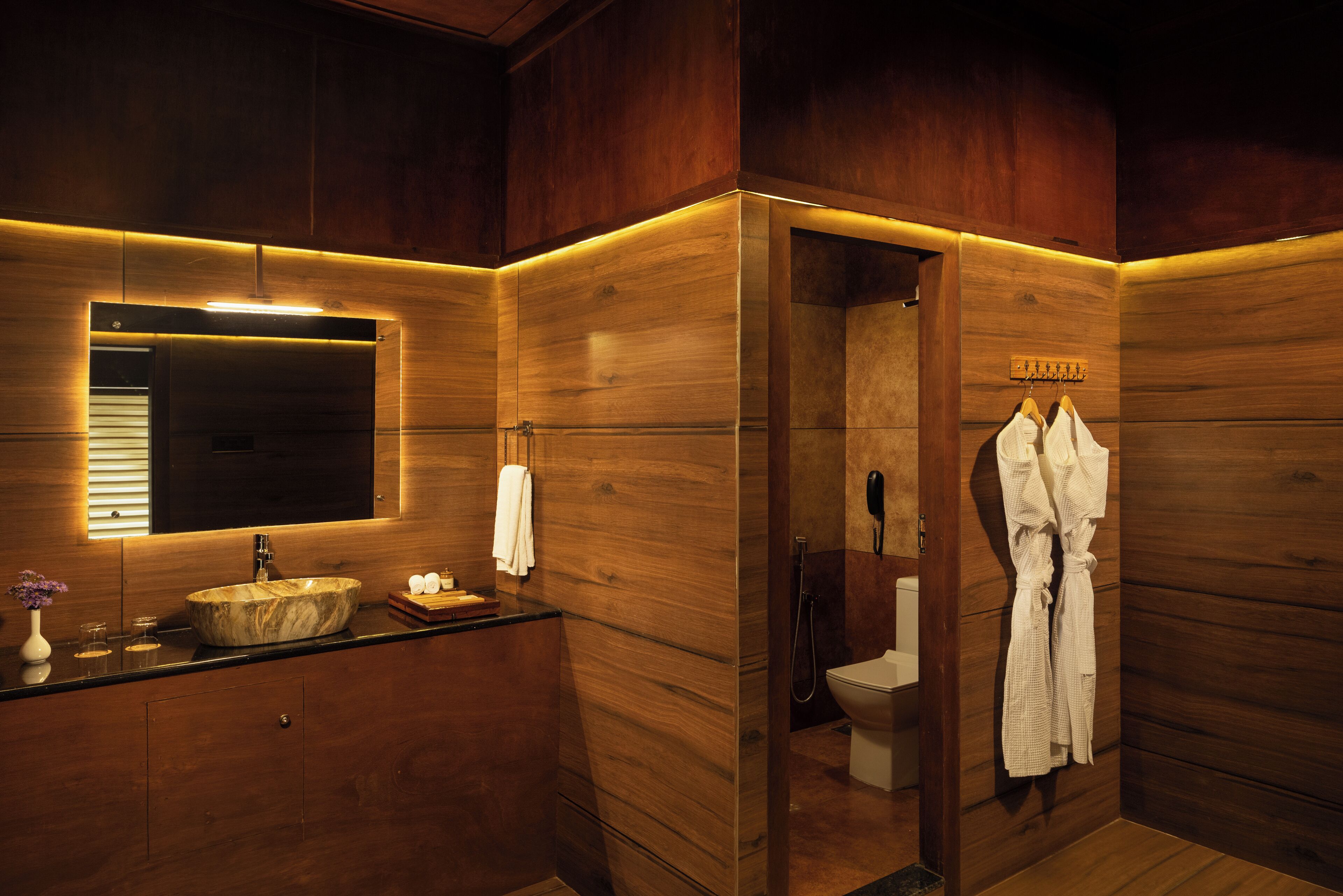 A wooden bathroom with a large mirror, a sink, and a toilet.