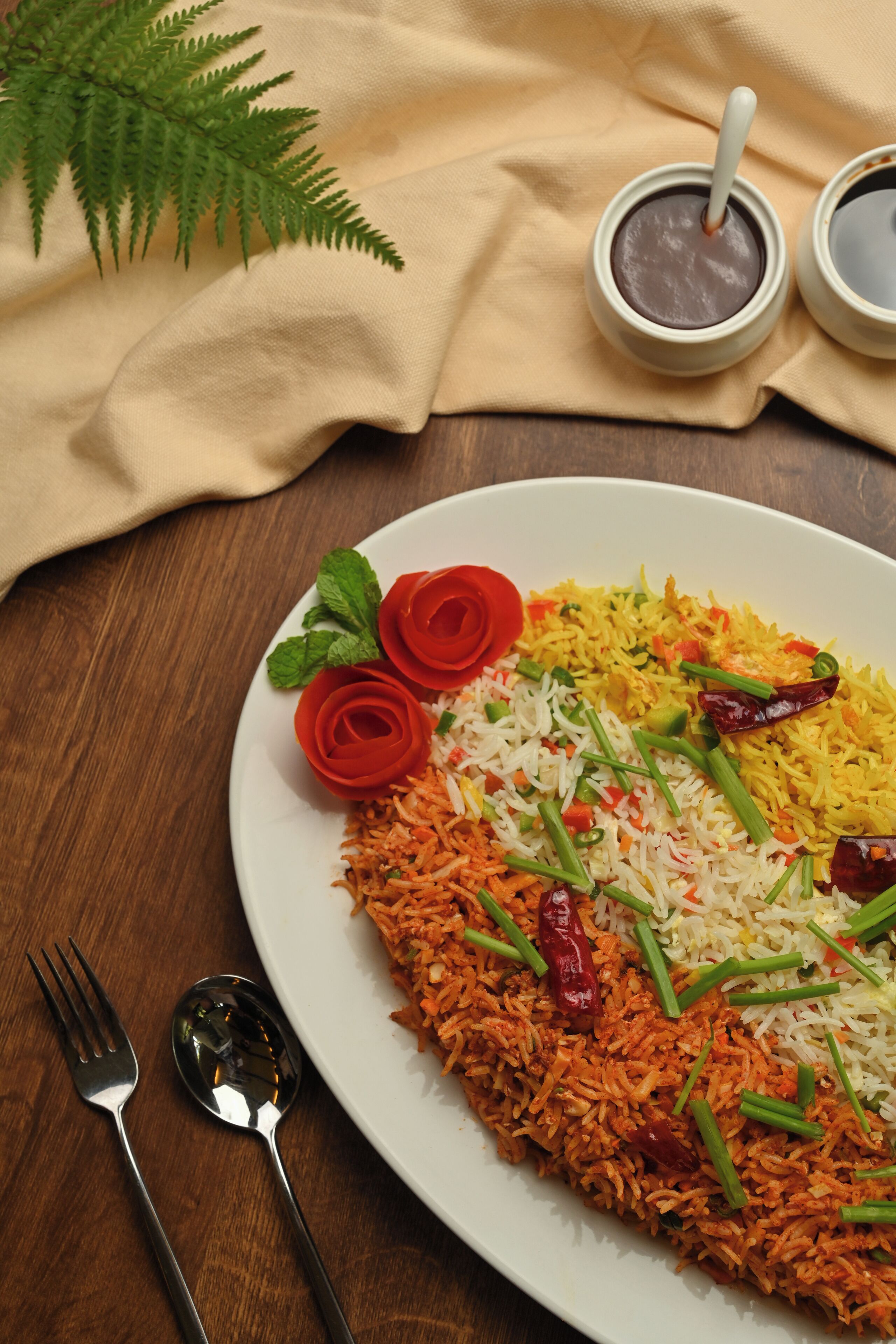 A plate of biryani with red and yellow rice, garnished with green onions and red chilies, on a wooden table.