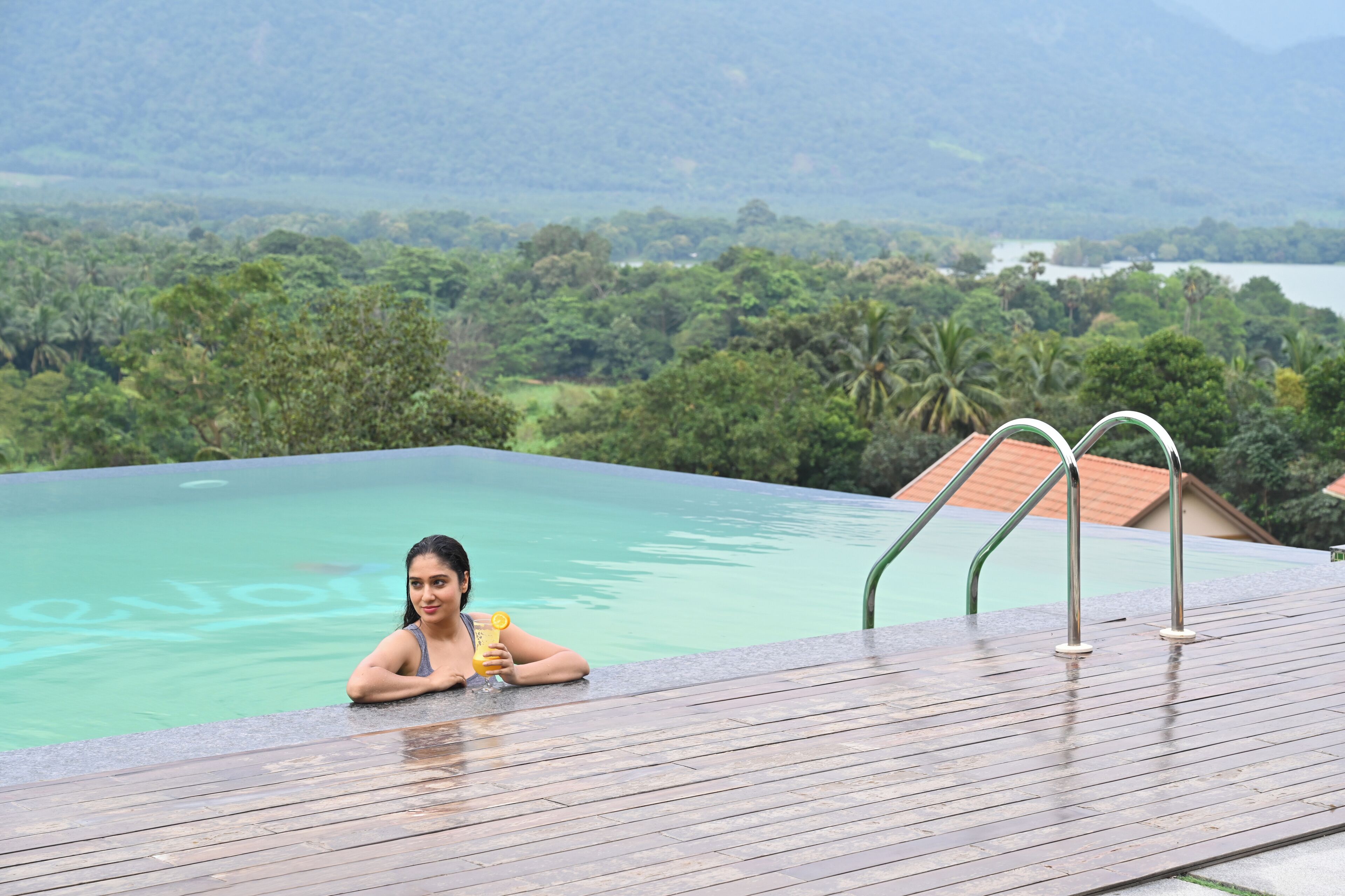 Una persona relajándose en una piscina con vistas a un paisaje exuberante y una masa de agua distante.
