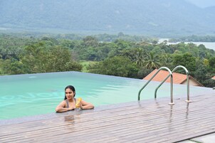 Una persona relajándose en una piscina con vistas a un paisaje exuberante y una masa de agua distante.