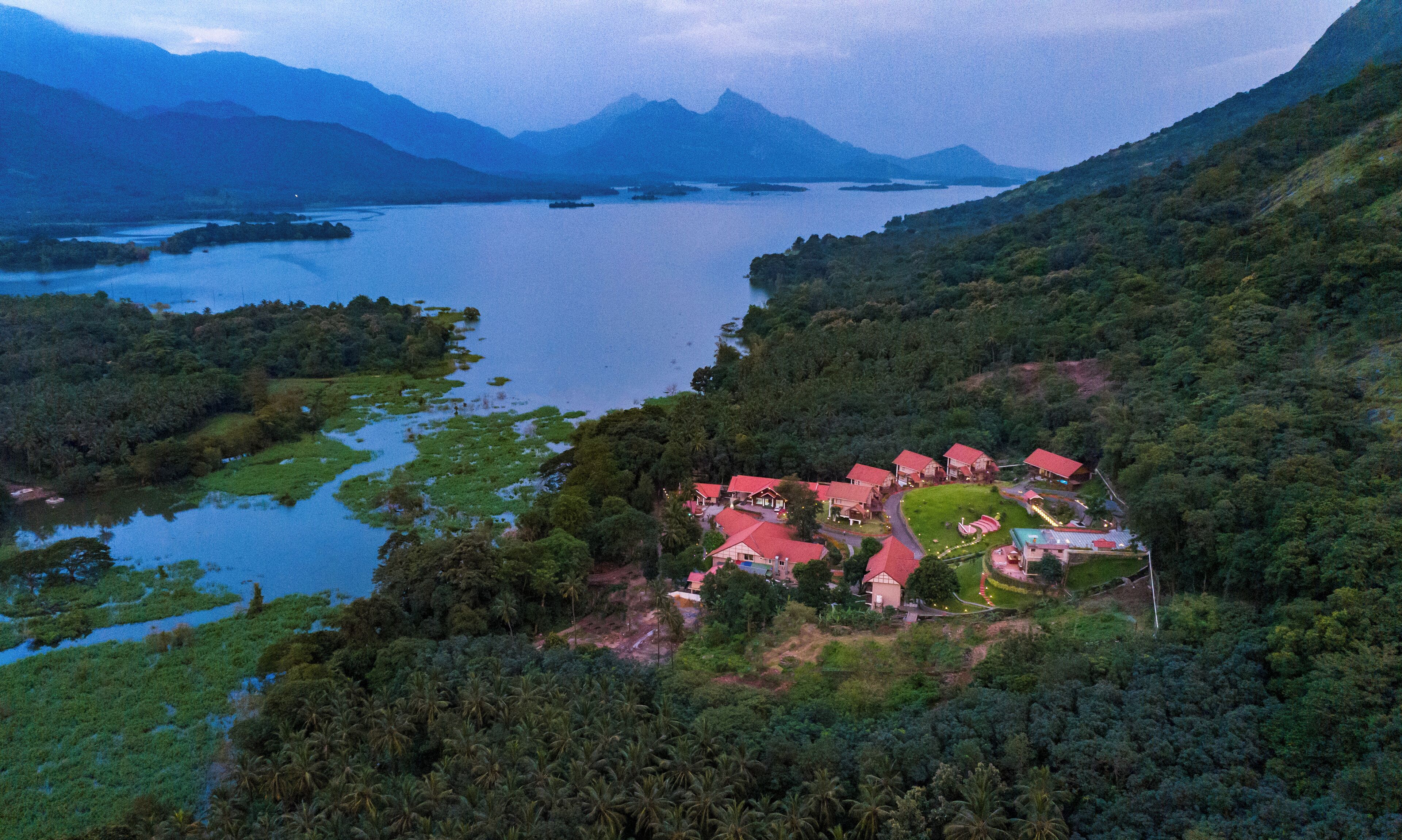 A resort with multiple red-roofed buildings surrounded by lush greenery and a lake.