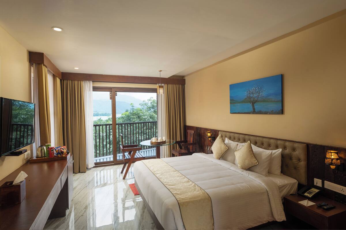 Une chambre d’hôtel avec un grand lit, une télévision, un balcon avec une table et des chaises, et un tableau au mur.