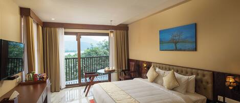 A hotel room with a large bed, a TV, a balcony with a table and chairs, and a painting on the wall.