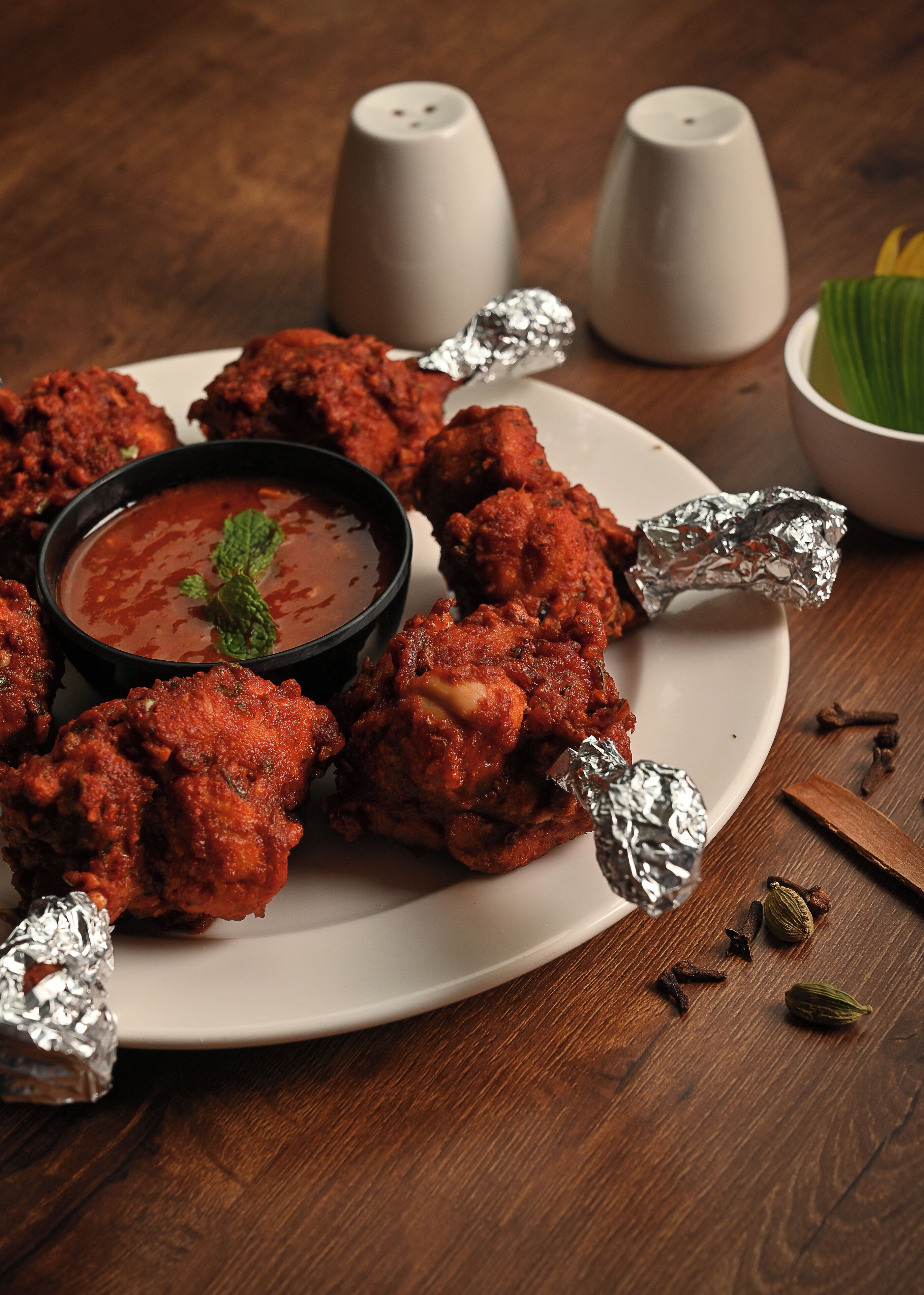 A plate of fried chicken with foil-wrapped pieces and a bowl of dipping sauce.