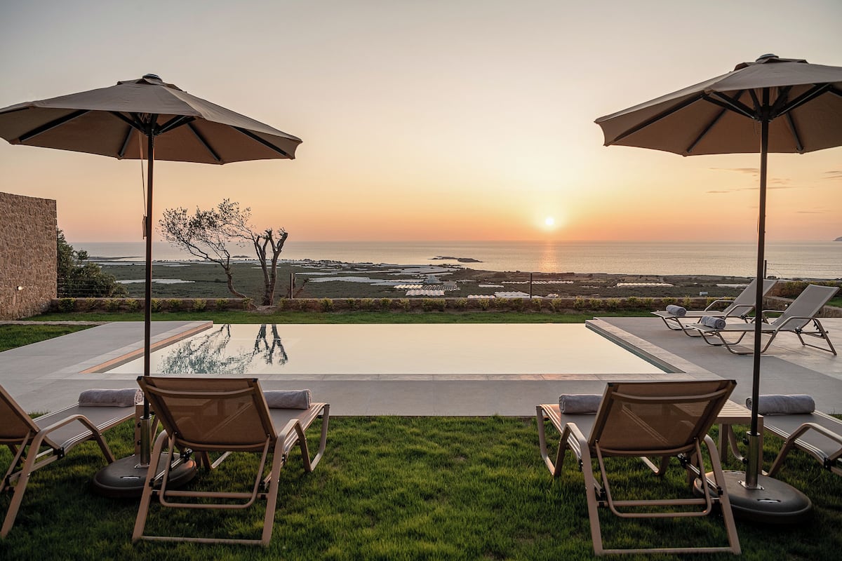 A poolside area with lounge chairs and umbrellas overlooking the ocean at sunset.