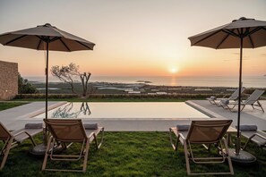 A poolside area with lounge chairs and umbrellas overlooking the ocean at sunset. - GG Villas (Kissamos)
