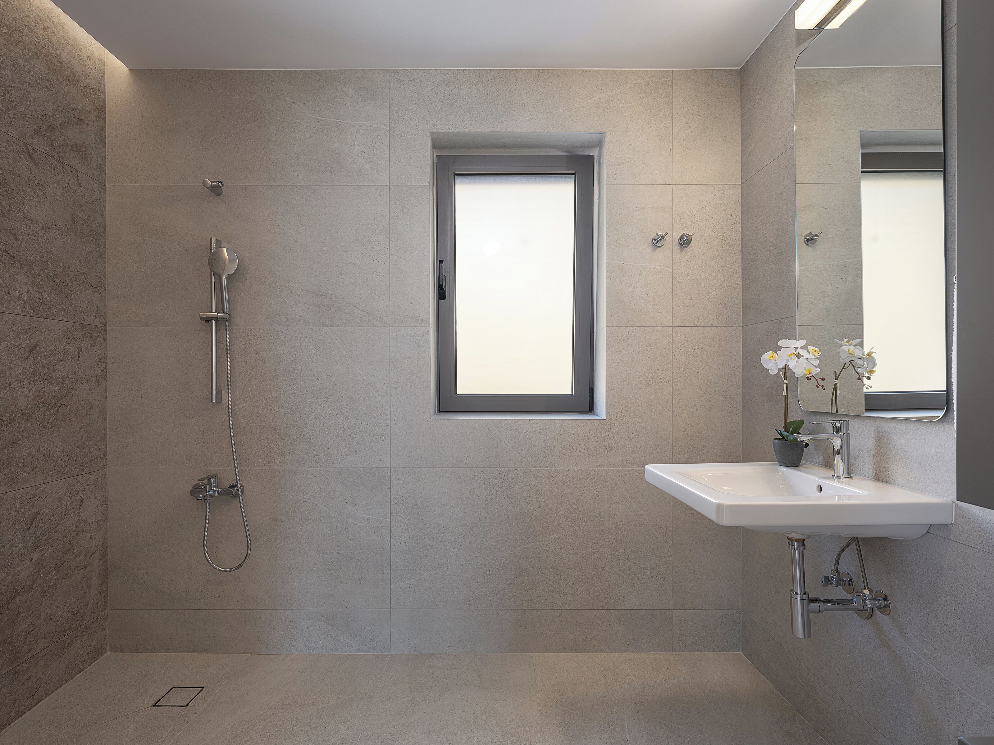 Un baño moderno con ducha, un ventanal pequeño y un lavamanos con espejo.
