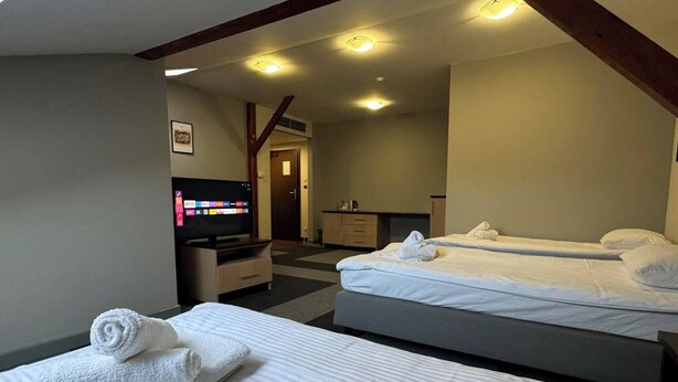 A hotel room with two beds, a TV, a small kitchenette, and a bathroom visible through an open door. - Magiczna Farma Mąka i Magia  (Zambrów)