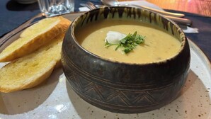 A bowl of soup with a garnish, accompanied by slices of bread on a plate, set on a table with a glass of water and a small bowl of coleslaw. - Magiczna Farma Mąka i Magia  (Zambrów)