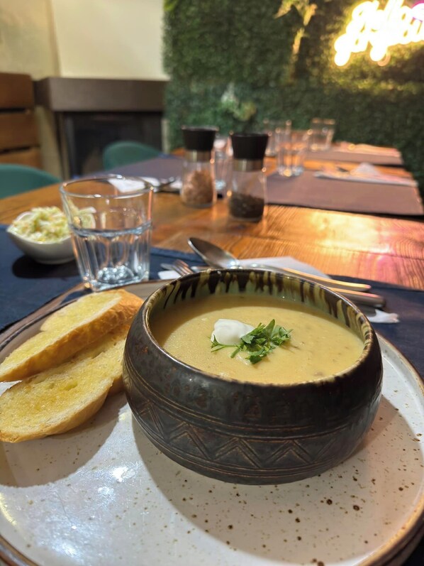 A bowl of soup with a garnish, accompanied by slices of bread on a plate, set on a table with a glass of water and a small bowl of coleslaw. - Magiczna Farma Mąka i Magia (Zambrów)