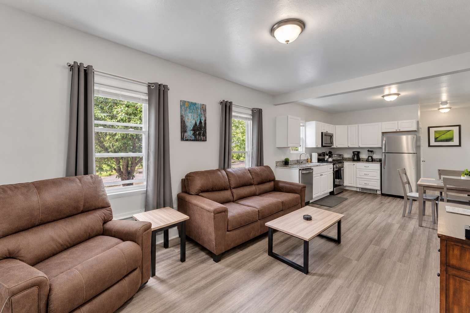 A modern living room with two sofas, a coffee table, and a kitchen area with white cabinets and appliances.