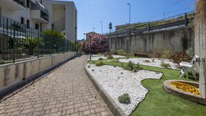 A courtyard with a paved walkway, a small garden with white gravel and green grass, and a white chair.