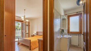 A bedroom with a bed, bedside table, and a window with a view of greenery.
