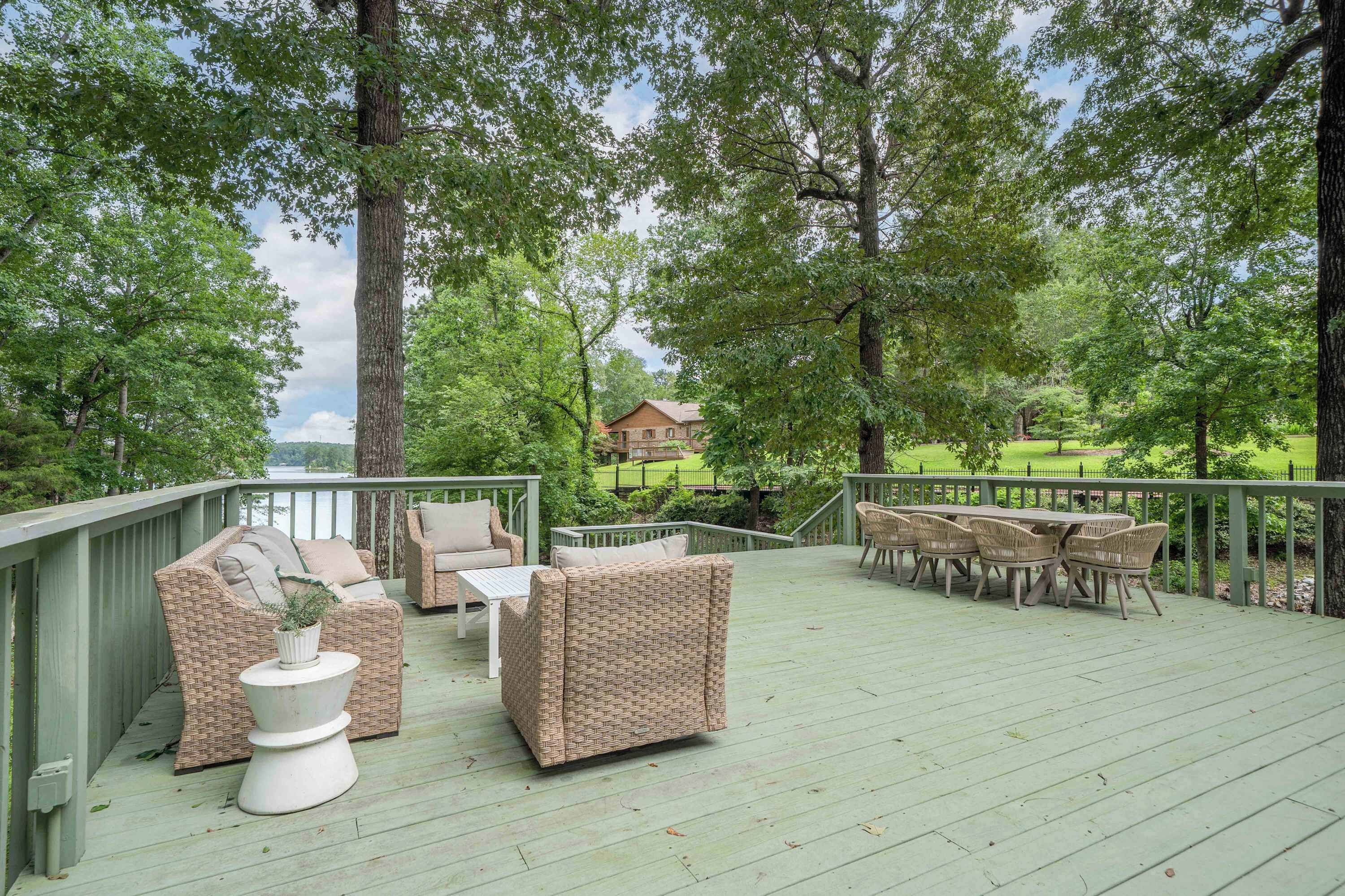 A deck with wicker furniture, a white table, and a view of a house in the background.