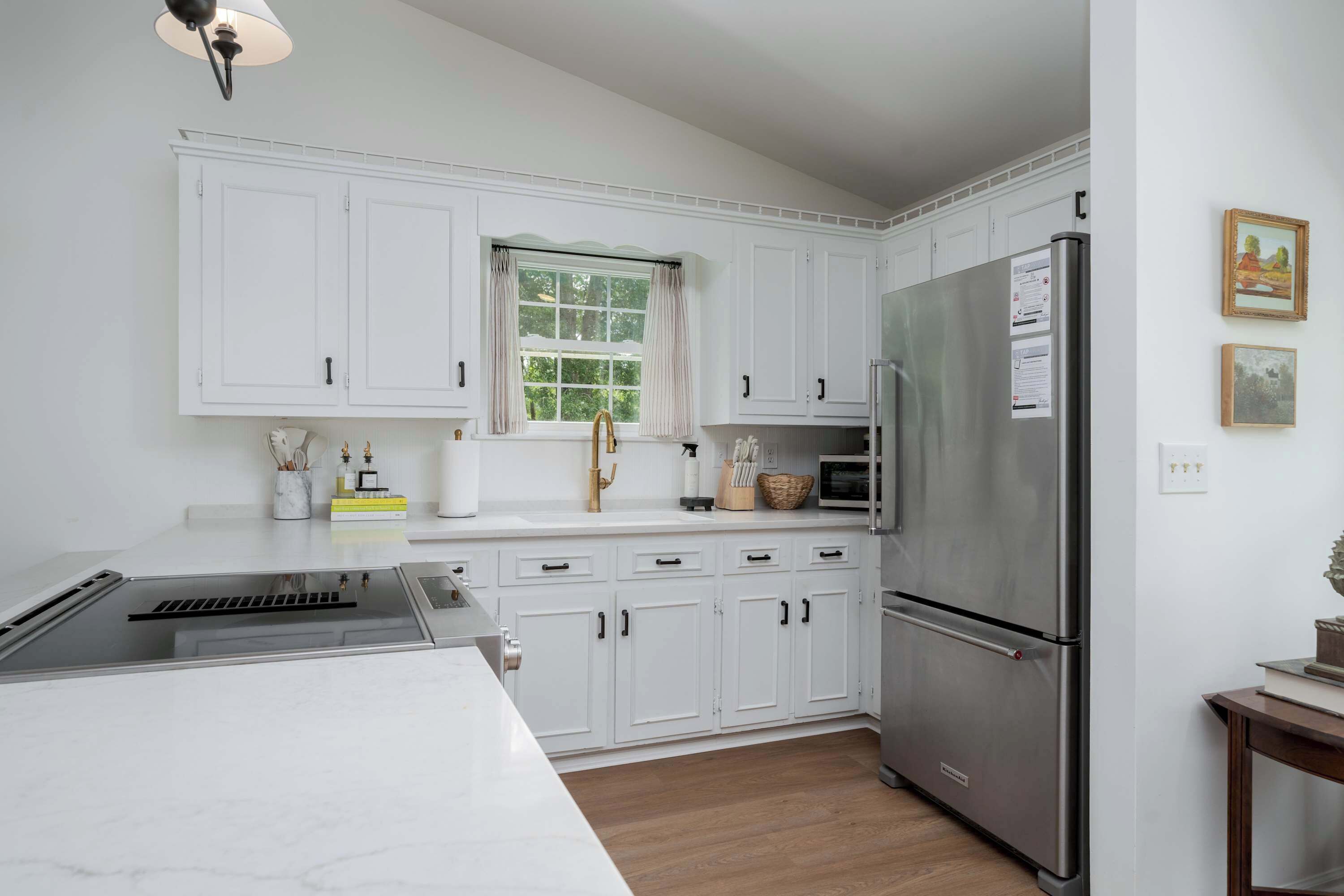 A modern kitchen with white cabinets, a stainless steel refrigerator, and a window with curtains.