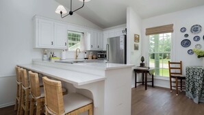 A modern kitchen with white cabinetry, a central island with bar stools, a stainless steel refrigerator, and a dining area with a table and chairs.