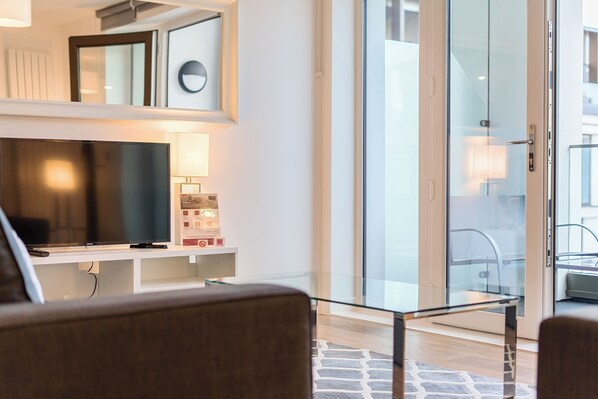 Una sala de estar moderna con una televisión de pantalla plana, una mesa de centro de vidrio y un sofá.