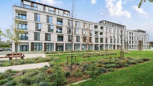 Un edificio moderno a più piani con tetto piatto, ampie finestre e un curato giardino con vialetti e panchine.