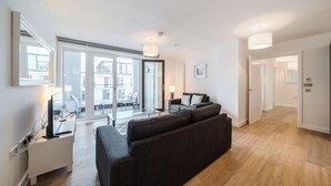 Un soggiorno moderno con un divano ampio, un tavolino in vetro e un portatile su un tavolino laterale. Si apre una porta su un balcone con vista sugli edifici.