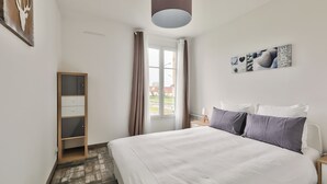 A bedroom with a large bed, a wardrobe, a window with curtains, and a wall with artwork.