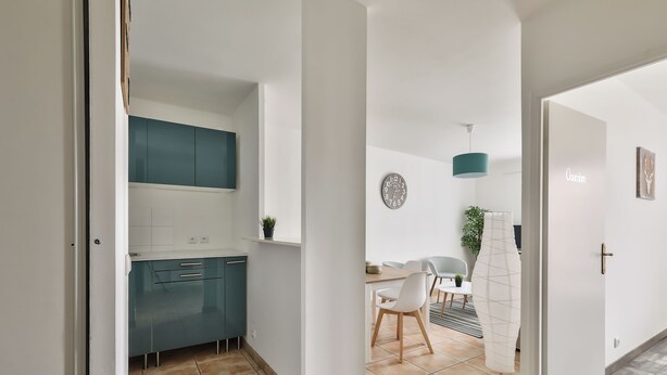 A modern kitchen with teal cabinets, a white countertop, and a dining area with a table and chairs.