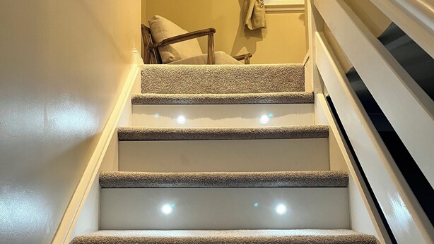 A carpeted staircase with a handrail, leading to a room with a chair and a window.