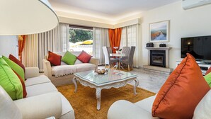 Ein modernes Wohnzimmer mit einem Glastisch, weißen Sofas und farbenfrohen Kissen.