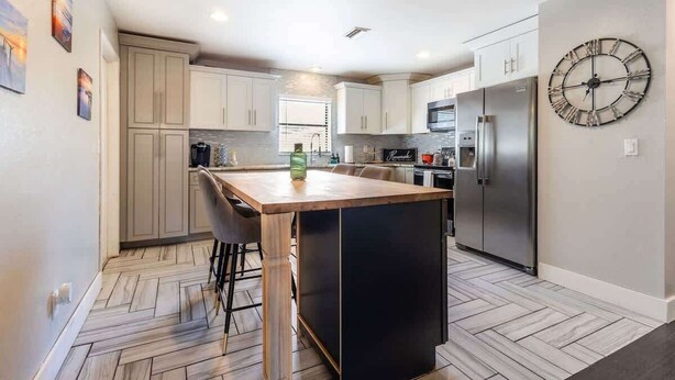 A modern kitchen with a central island, stainless steel appliances, and a large wall clock. - Spacious 3-BR Home with Patio, Firepit & BBQ! (Largo)