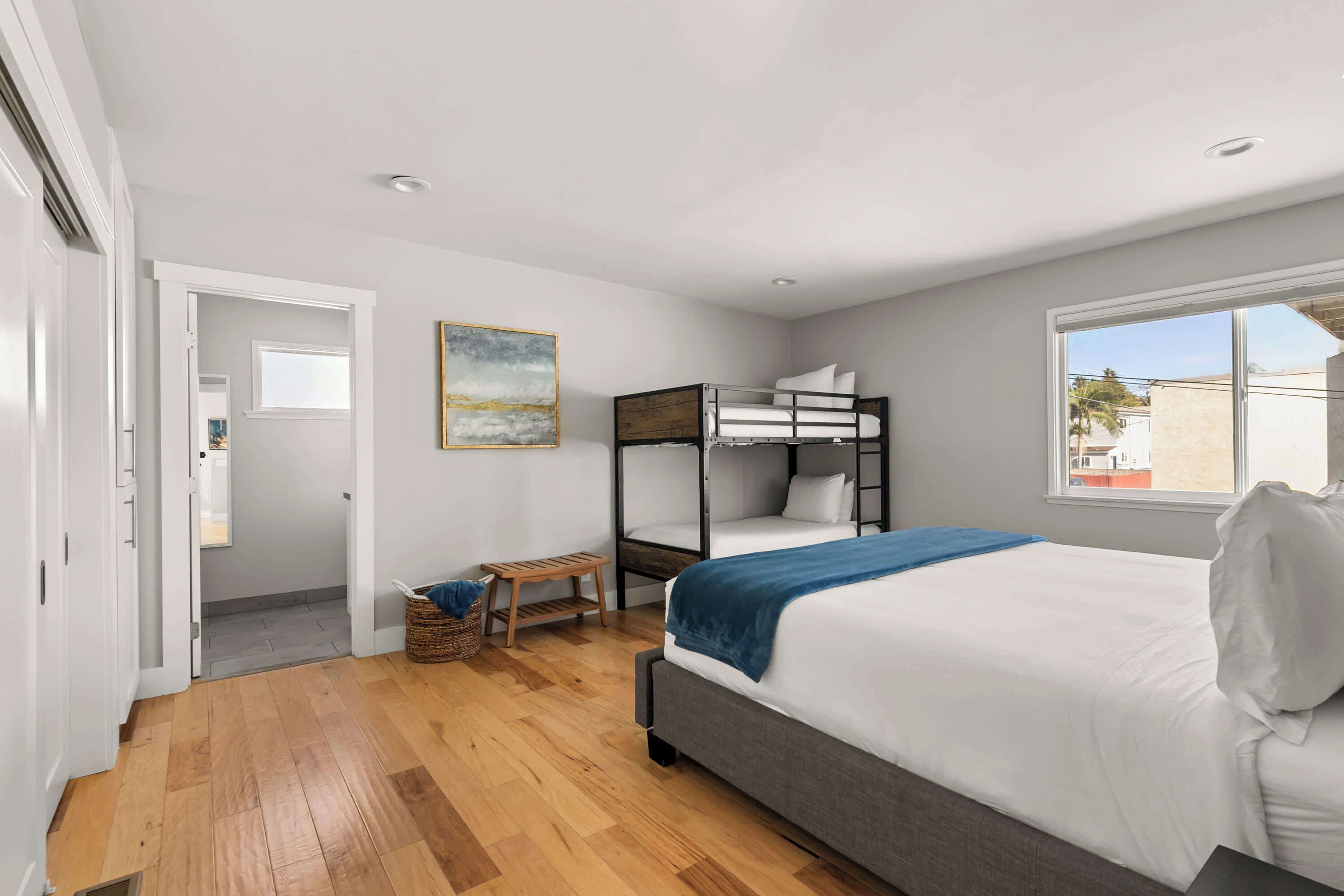 Een slaapkamer met een stapelbed, een enkel bed, een raam en een schilderij aan de muur.