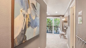 A hallway with a large abstract painting, a door with a coat rack, and a view to a balcony with outdoor furniture. - Modern 2BR/2BA Kirkland Home, Walk to Beach Park (Kirkland)