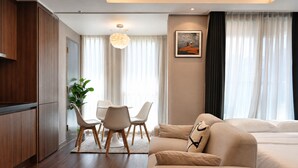 A modern hotel room with a wooden wardrobe, a dining table with chairs, a sofa, a large window with curtains, and a painting on the wall. - Haeundae Lamer Stay (Busan)