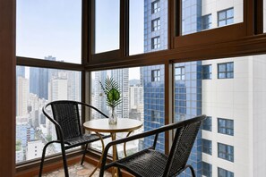 A room with a view of a cityscape through large windows, a round table, and two chairs.