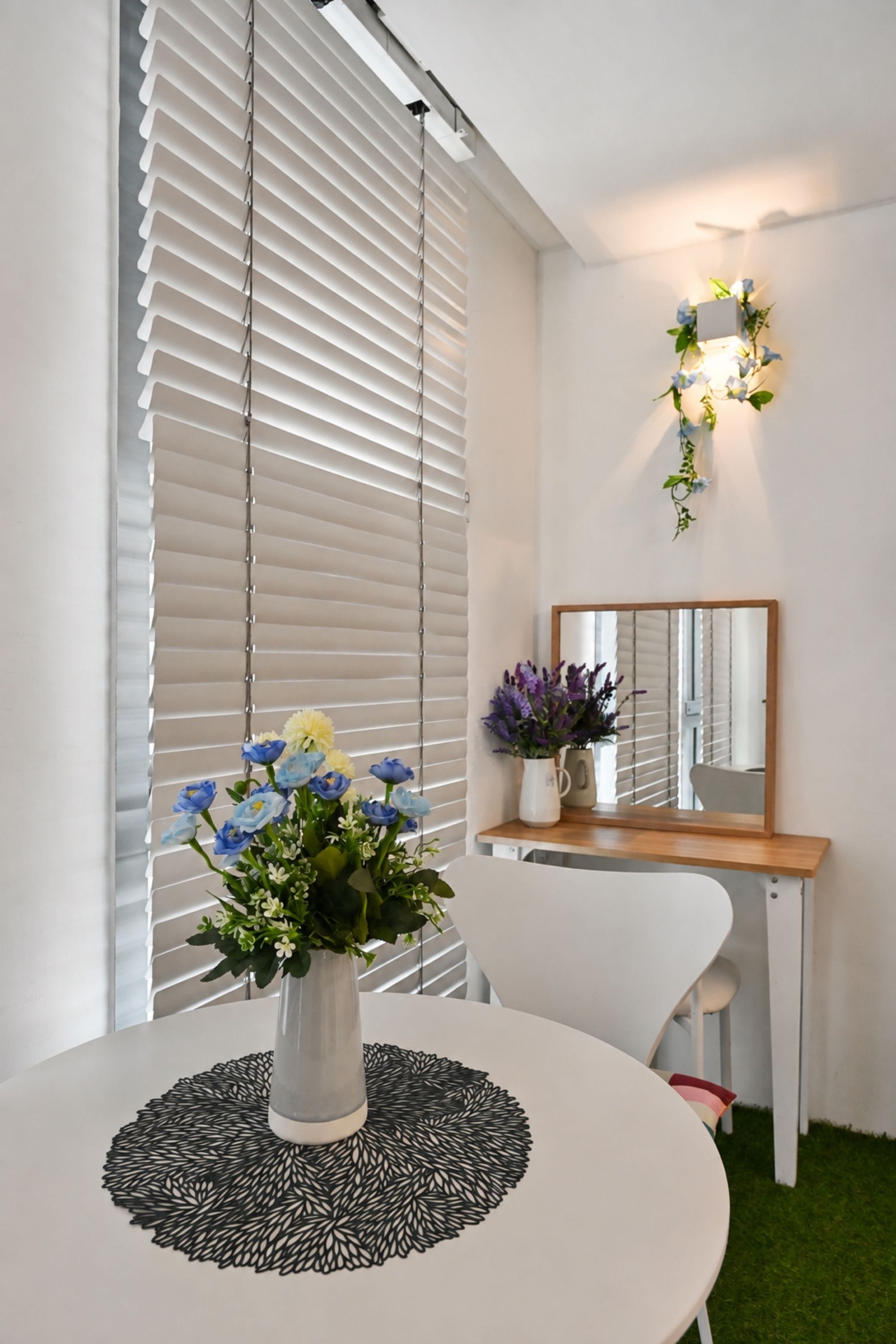 Ett rum med ett runt bord, en vas med blommor, en spegel och en väggmonterad lampa.
